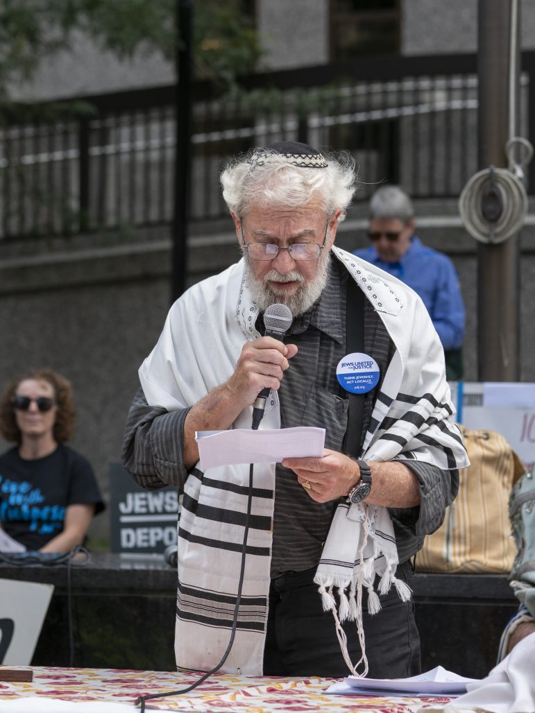 Rabbi David Shneyer speaking with a mic at our Tisha B'Av event. He wears a tallit and kippeh.